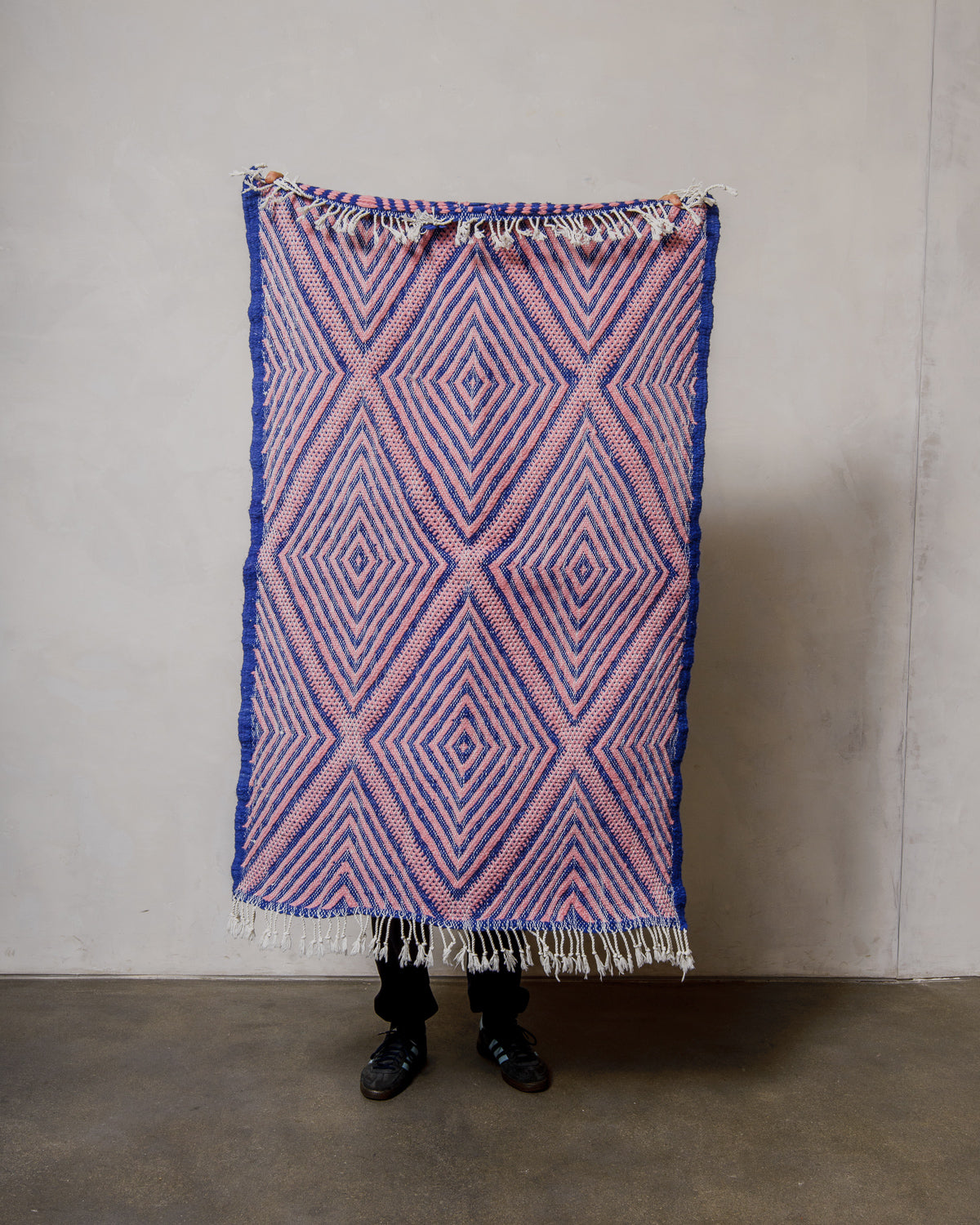 Person holding a blue and pink patterned Berberlin Kelim rug against a plain background